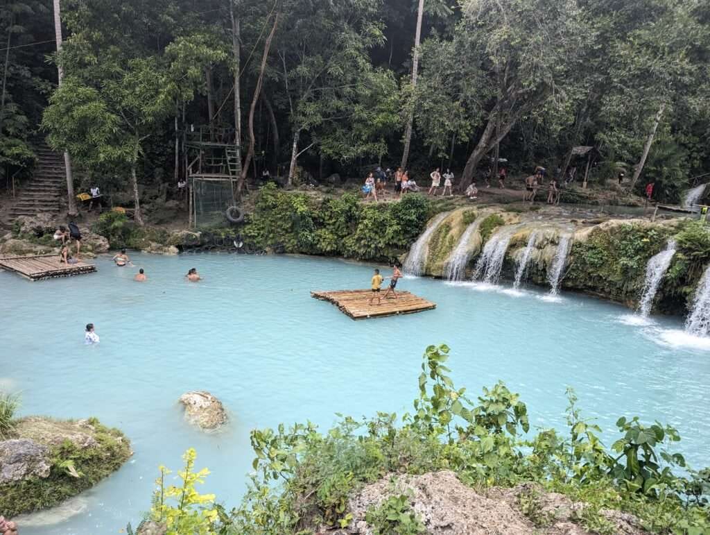 Cambugahay Falls: Complete Siquijor Island Waterfall Guide 2 Crystal clear water cascades over three tiers of lush greenery at Cambugahay Falls. Sunlight filters through the trees, casting a warm glow on the serene pool below